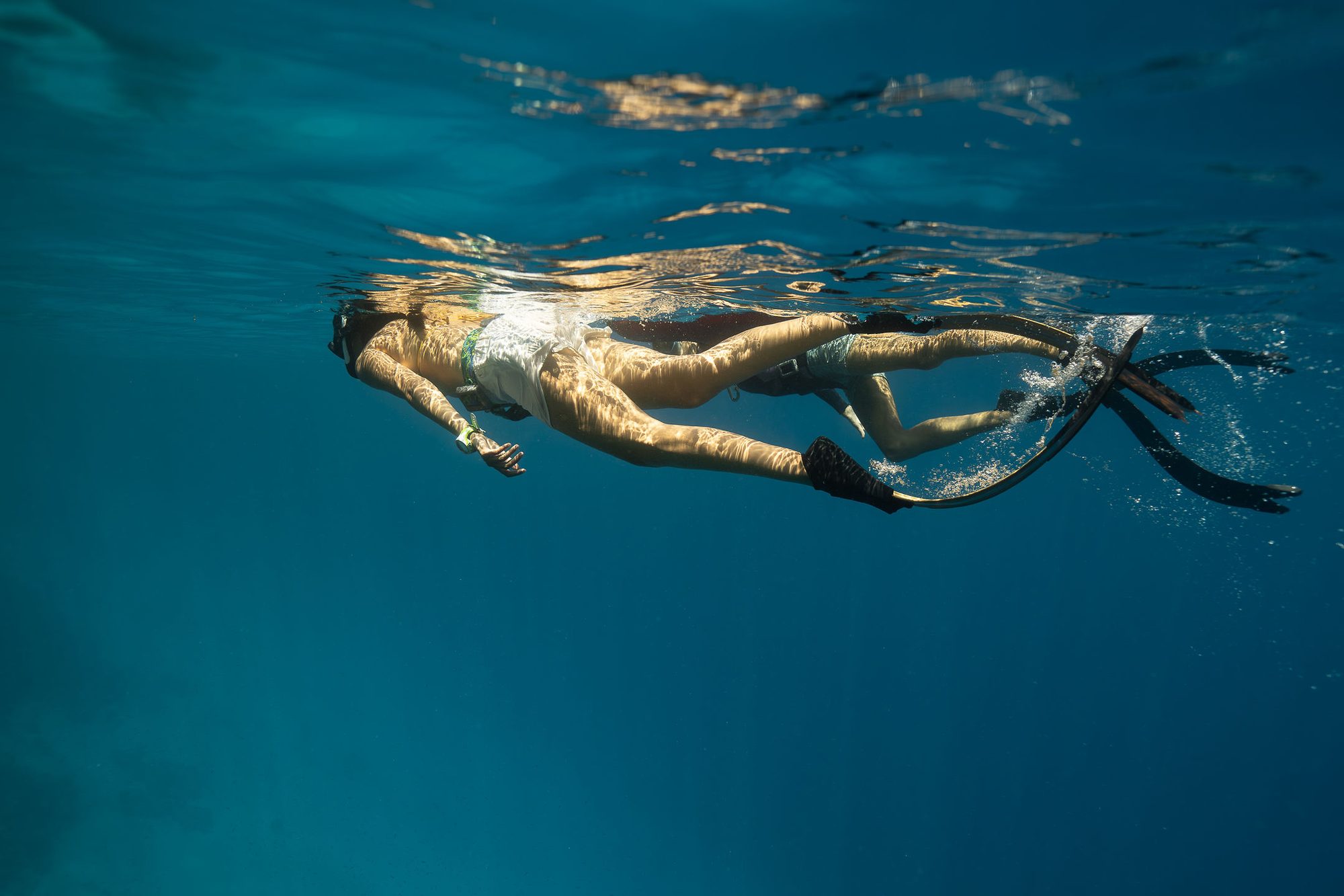 Two freedivers finning side by side just beneath the sunlit surface of the Red Sea